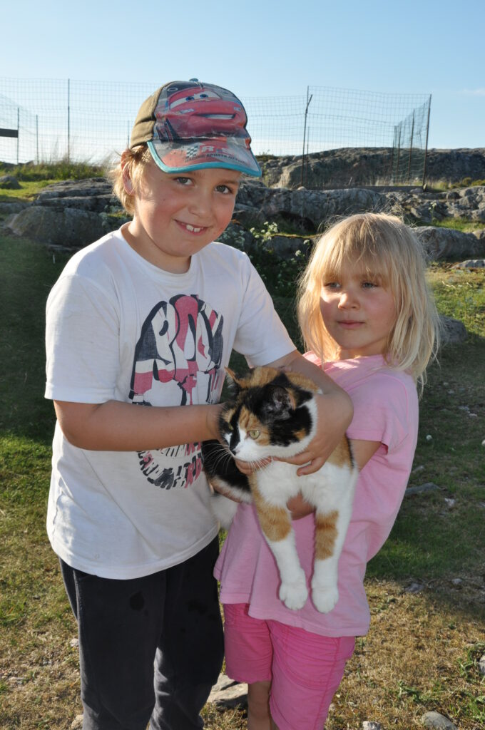 Två barn ute som håller i en katt.