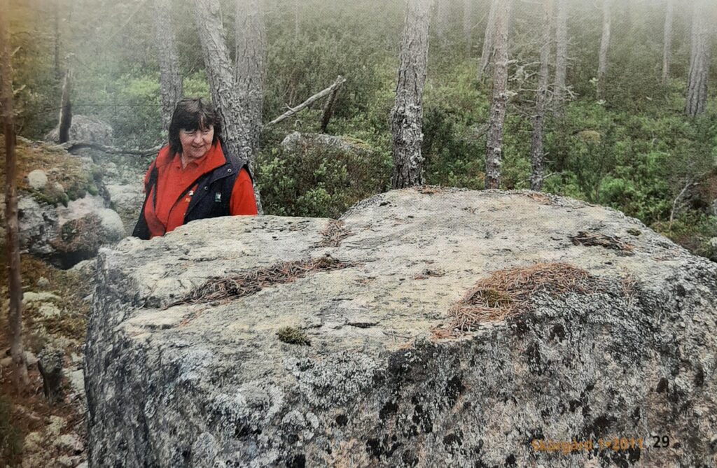 Kvinna i skogen vid en stor sten.