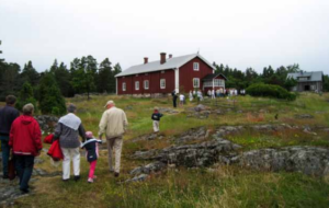 Rött hus på en klippa med barn och vuxna som går mot det.