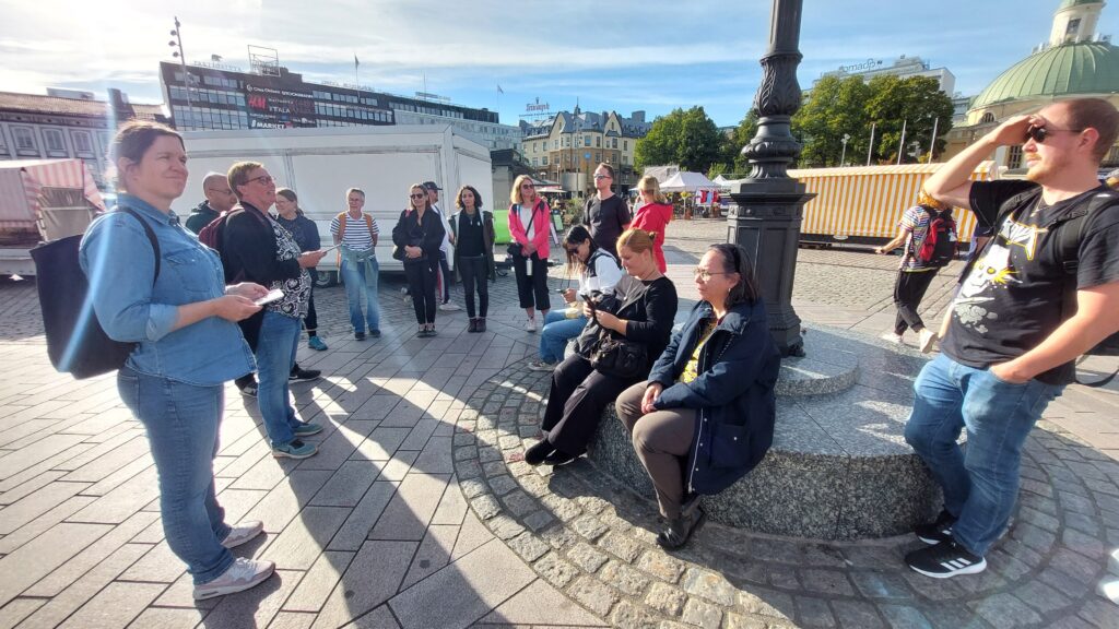 En grupp människor sitter och står samlade på Salutroget i Åbo i vackert solsken.